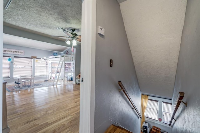 stairway with wood finished floors, a textured ceiling, ceiling fan, and a textured wall