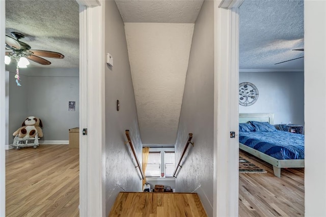 stairs featuring baseboards, a textured ceiling, ceiling fan, and wood finished floors