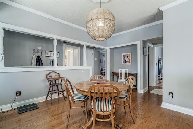 dining space with visible vents, a textured ceiling, wood finished floors, crown molding, and baseboards