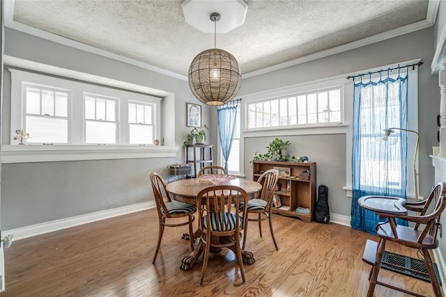 dining space featuring light wood-type flooring, plenty of natural light, a textured ceiling, and ornamental molding