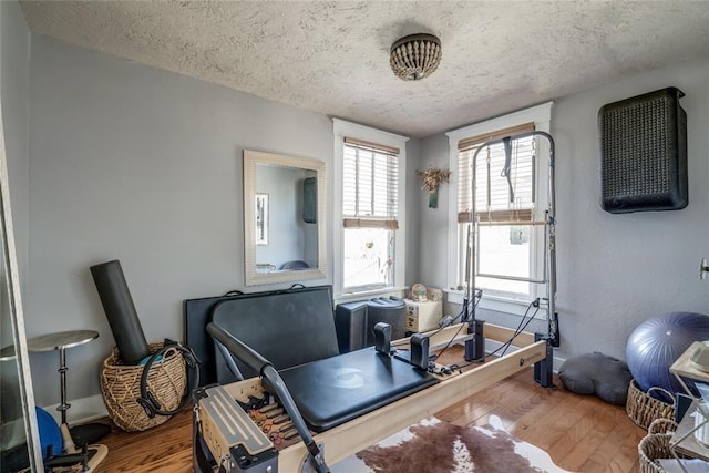 workout area featuring baseboards, a textured ceiling, and wood finished floors