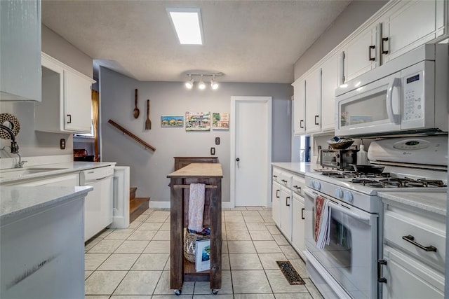 kitchen featuring a sink, white cabinetry, white appliances, light tile patterned flooring, and baseboards