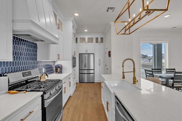 kitchen featuring crown molding, premium range hood, light wood-type flooring, appliances with stainless steel finishes, and a sink