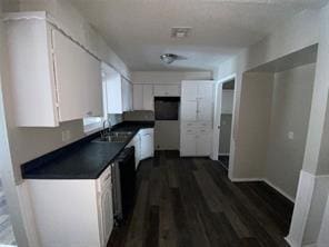 kitchen featuring visible vents, a sink, dark countertops, dark wood-style floors, and white cabinetry