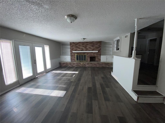 unfurnished living room featuring built in shelves, dark wood-style floors, french doors, a textured ceiling, and a brick fireplace