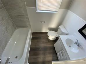 bathroom featuring vanity, wood finished floors, vaulted ceiling, toilet, and a washtub