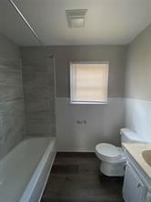 bathroom with toilet, wood finished floors, wainscoting, shower / bath combination, and vanity