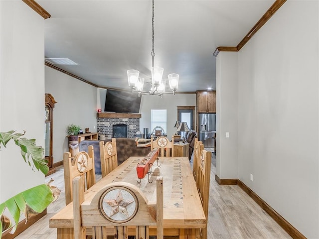 dining area with visible vents, crown molding, a brick fireplace, light wood-type flooring, and a chandelier