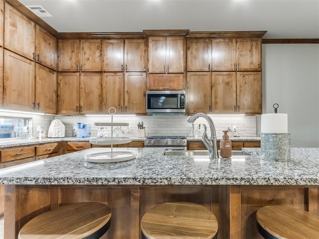 kitchen with brown cabinetry, a sink, decorative backsplash, stainless steel appliances, and a kitchen breakfast bar