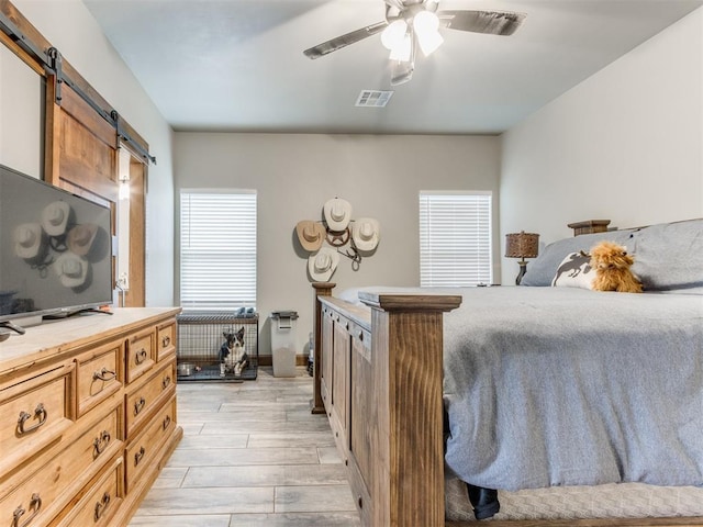 bedroom featuring light wood finished floors, visible vents, a ceiling fan, and a barn door