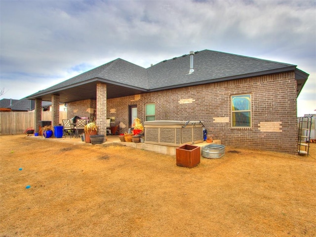 rear view of property featuring a patio, fence, brick siding, and roof with shingles