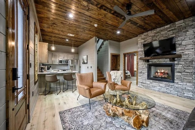 living room featuring stairway, a ceiling fan, a fireplace, wood ceiling, and light wood-style floors