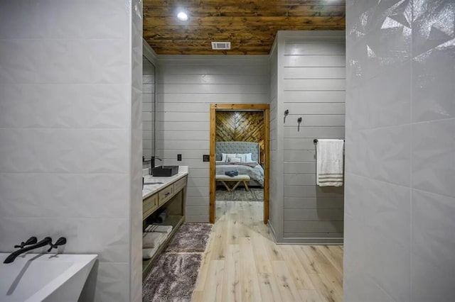 ensuite bathroom featuring visible vents, ensuite bathroom, wood finished floors, a soaking tub, and a sink