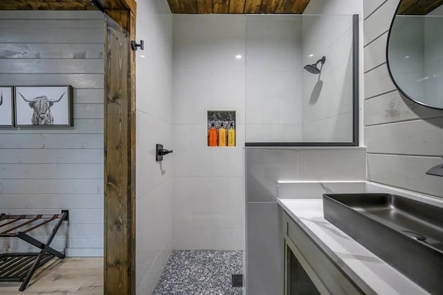 bathroom with tiled shower, wood walls, and vanity