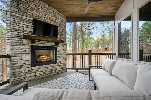 sunroom with plenty of natural light, wood ceiling, an outdoor stone fireplace, and a ceiling fan