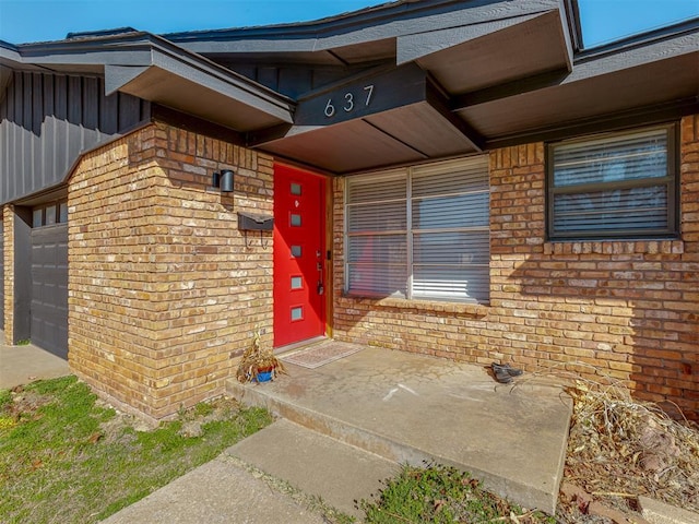 property entrance featuring a garage, brick siding, and board and batten siding