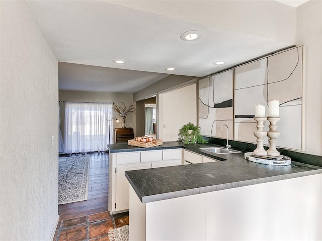 kitchen with dark countertops, recessed lighting, a peninsula, white cabinetry, and a sink