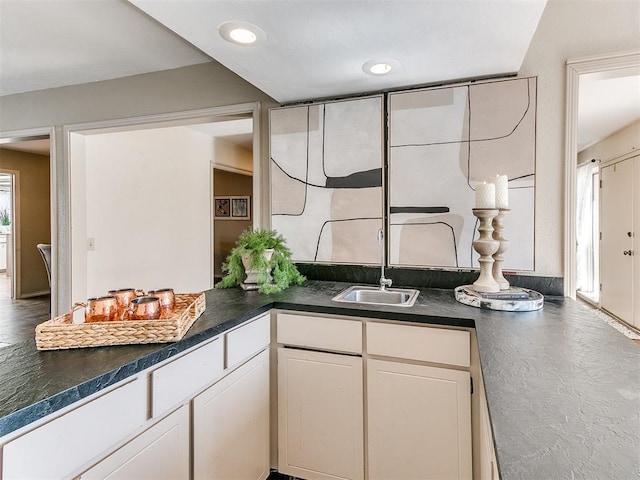 kitchen with dark countertops, recessed lighting, white cabinets, and a sink