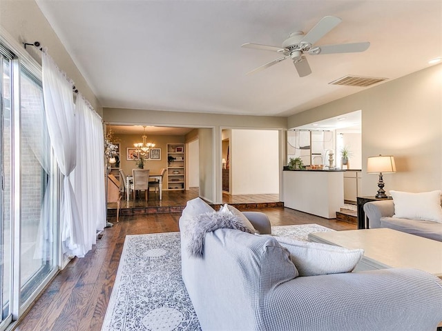 living area with dark wood-type flooring, ceiling fan with notable chandelier, visible vents, and a wealth of natural light