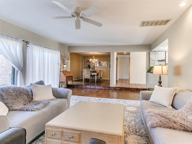 living area featuring ceiling fan with notable chandelier, wood finished floors, and visible vents