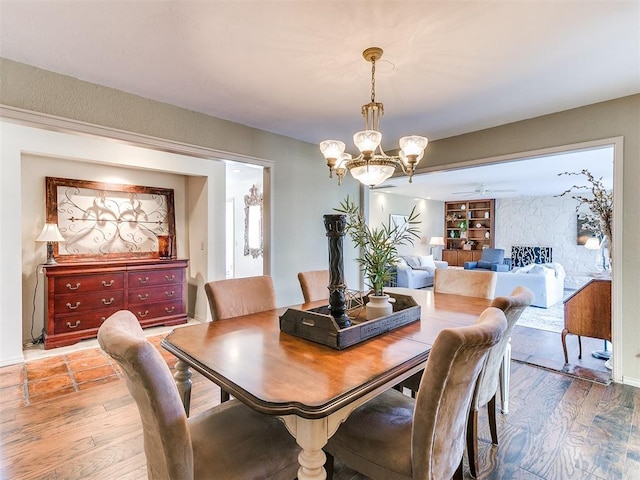 dining space featuring ceiling fan with notable chandelier, built in shelves, and wood finished floors