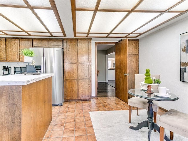 kitchen with brown cabinetry, light tile patterned flooring, light stone countertops, and stainless steel fridge with ice dispenser