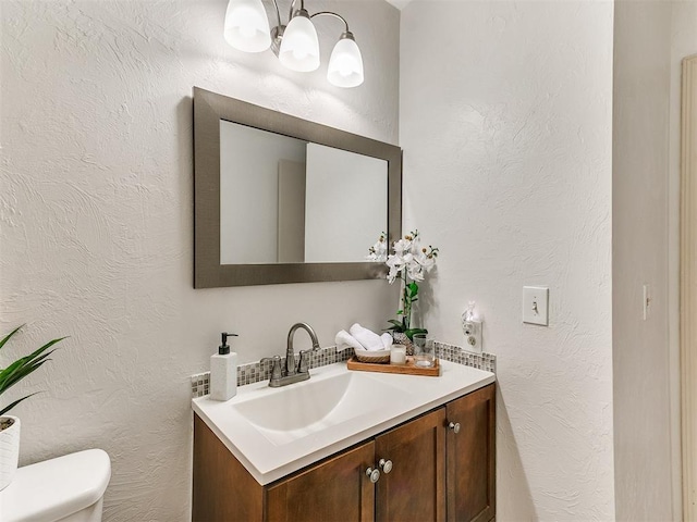 half bathroom featuring vanity, toilet, a textured wall, and a chandelier