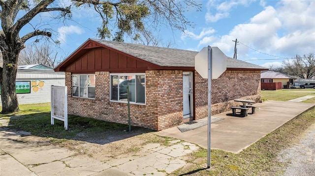 view of home's exterior with brick siding, board and batten siding, roof with shingles, a lawn, and a patio area