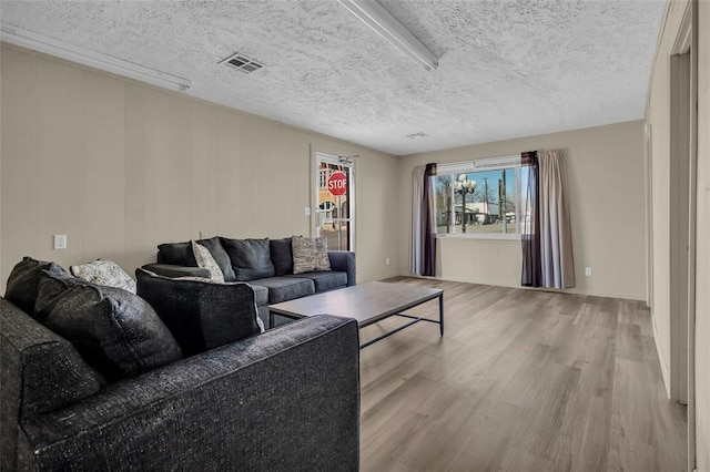 living room featuring visible vents, light wood-type flooring, and a textured ceiling