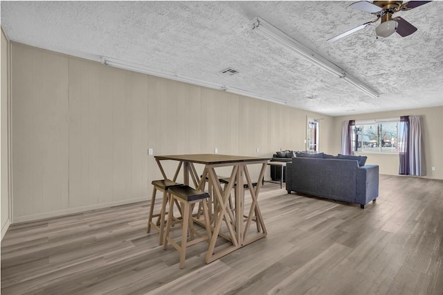 dining room featuring visible vents, a textured ceiling, wood finished floors, and a ceiling fan