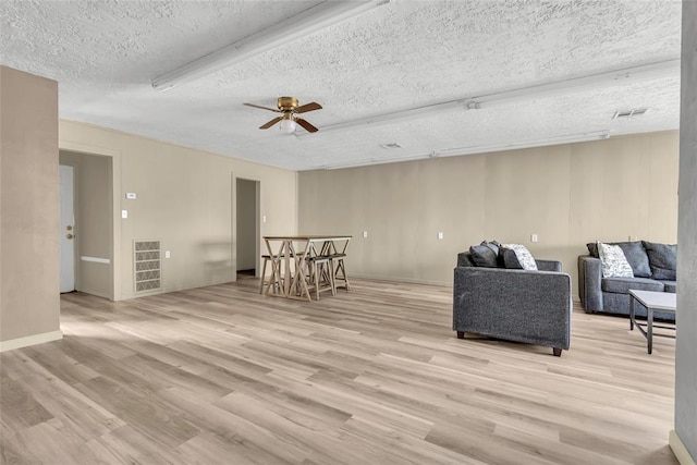 living area featuring light wood-type flooring, visible vents, a textured ceiling, and ceiling fan