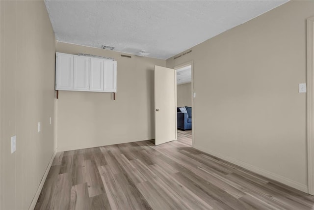 empty room with visible vents, baseboards, light wood-style floors, and a textured ceiling