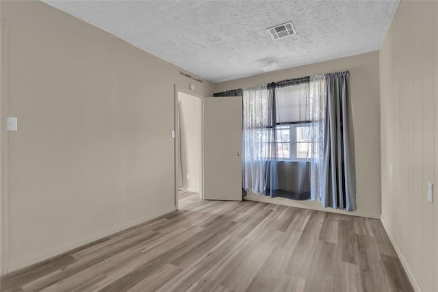 spare room featuring baseboards, wood finished floors, visible vents, and a textured ceiling