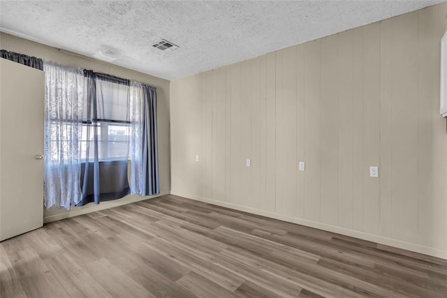 empty room with baseboards, wood finished floors, visible vents, and a textured ceiling