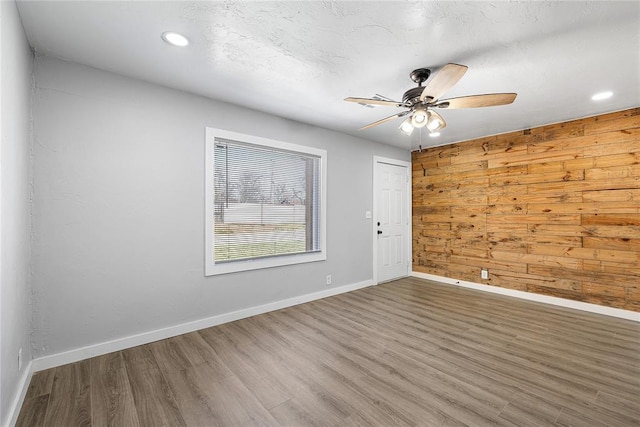 empty room featuring wood finished floors, a ceiling fan, baseboards, recessed lighting, and wood walls