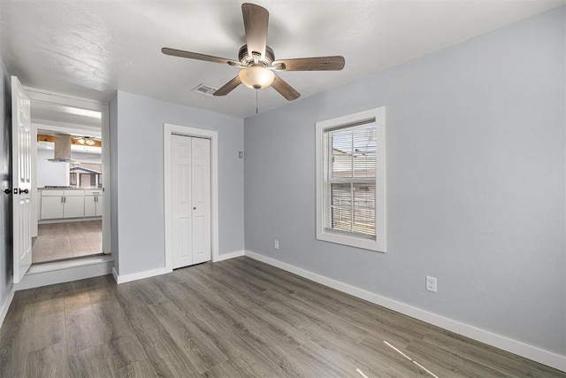 unfurnished bedroom featuring wood finished floors, visible vents, baseboards, ceiling fan, and a closet