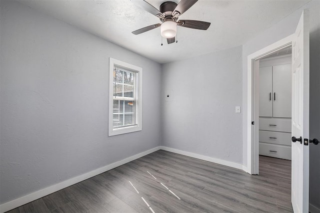 unfurnished room featuring wood finished floors, baseboards, a textured wall, and ceiling fan