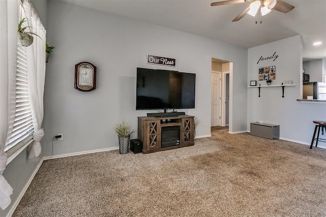 carpeted living area with baseboards and ceiling fan