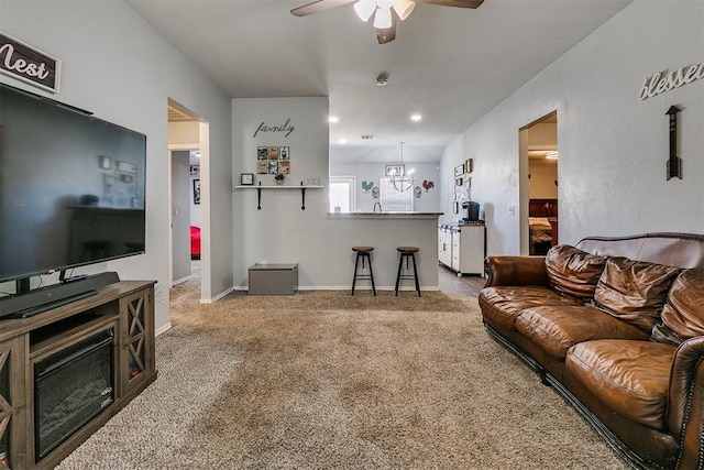 living area featuring ceiling fan with notable chandelier, baseboards, and carpet