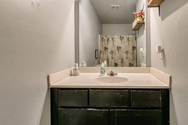 bathroom featuring a shower with shower curtain, visible vents, vanity, and a textured wall