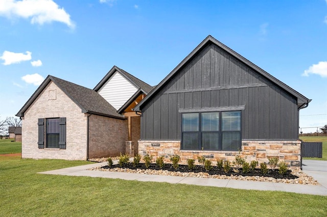 modern farmhouse style home featuring stone siding, board and batten siding, a front yard, and a shingled roof