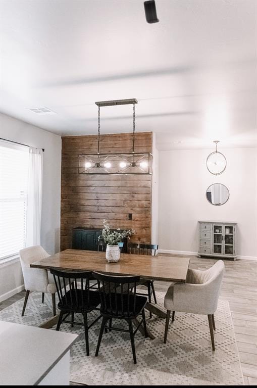 dining space featuring visible vents, wooden walls, light wood finished floors, baseboards, and an accent wall