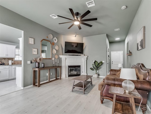 living room featuring a glass covered fireplace, visible vents, ceiling fan, and light wood finished floors