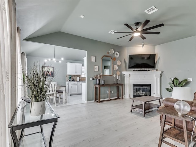 living room featuring visible vents, vaulted ceiling, light wood-style flooring, a glass covered fireplace, and a ceiling fan