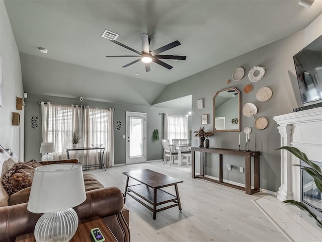 living area with baseboards, visible vents, light wood-style flooring, ceiling fan, and vaulted ceiling