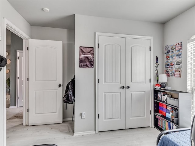 bedroom with light wood-style flooring, baseboards, and a closet