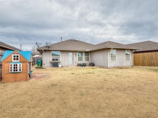 back of house with a shed, fence, a yard, roof with shingles, and an outdoor structure