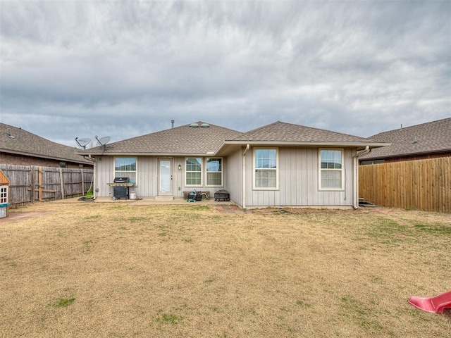 rear view of property with a fenced backyard, a lawn, and a shingled roof