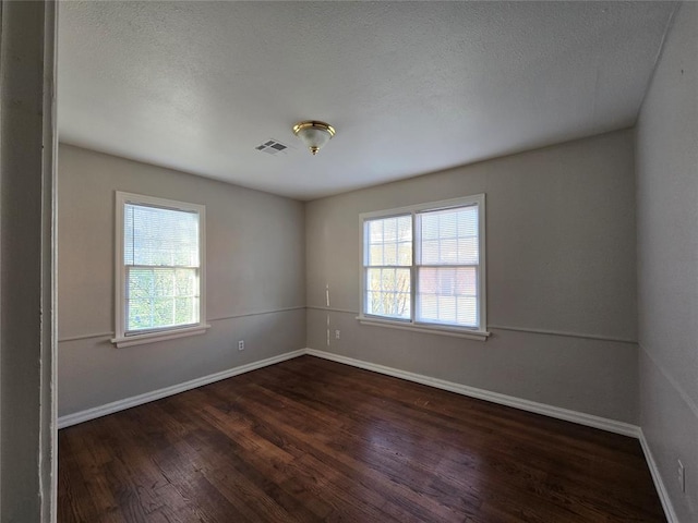 empty room with visible vents, a textured ceiling, baseboards, and wood finished floors