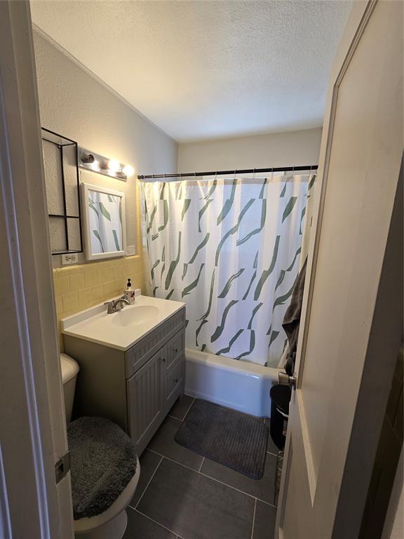 full bath with toilet, shower / bath combination with curtain, a textured ceiling, tile patterned flooring, and vanity